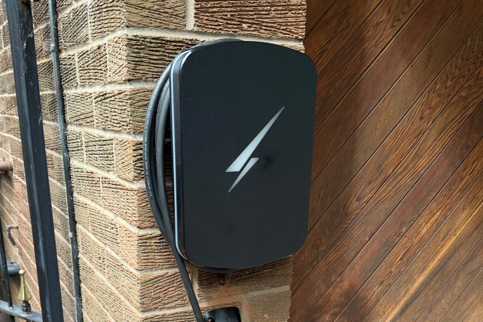 Tesla Wall Connector mounted on a brick exterior wall beside a wooden door