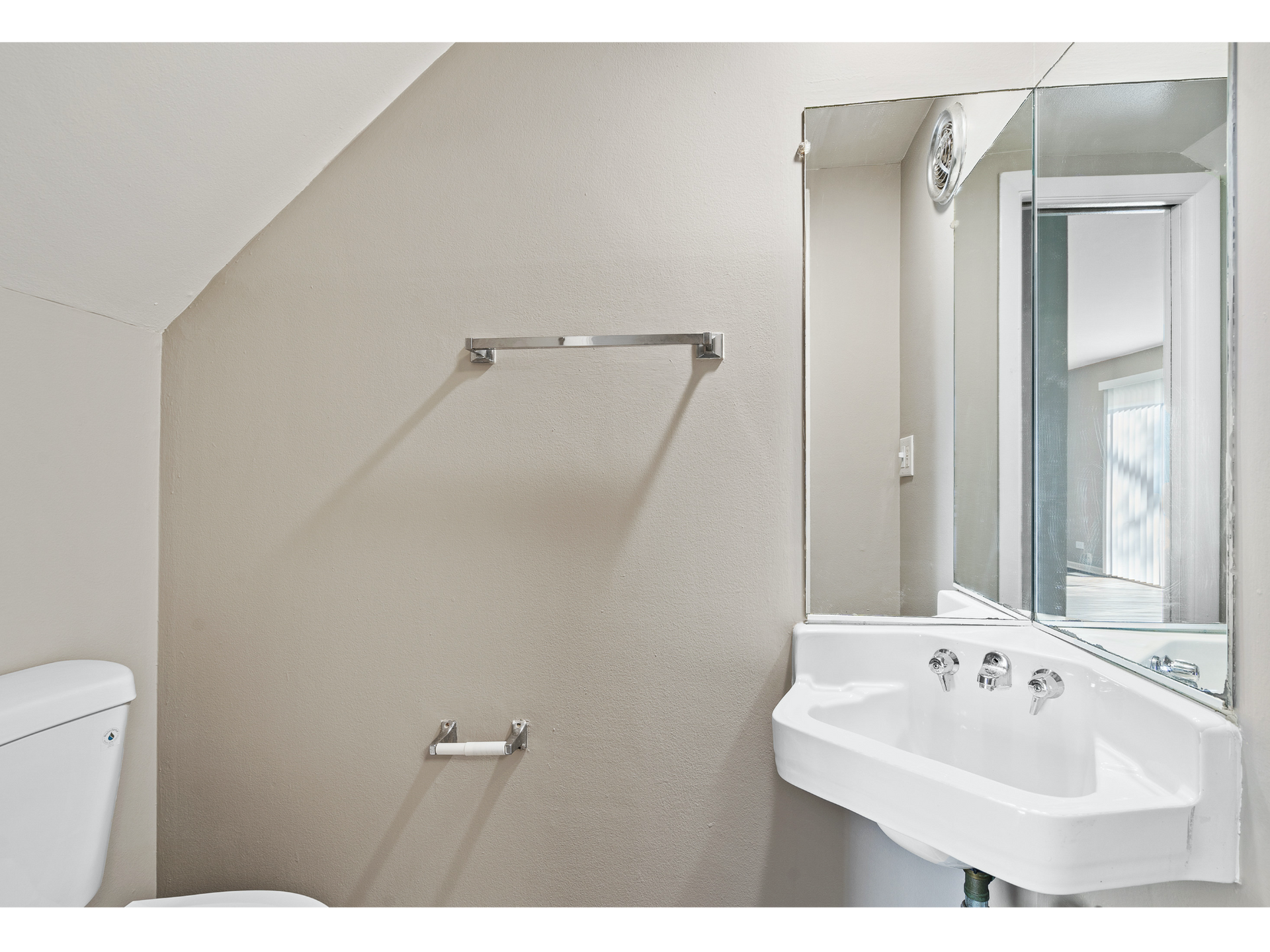 Small bathroom with a sink, mirror cabinet, towel bars, and a toilet partially visible.