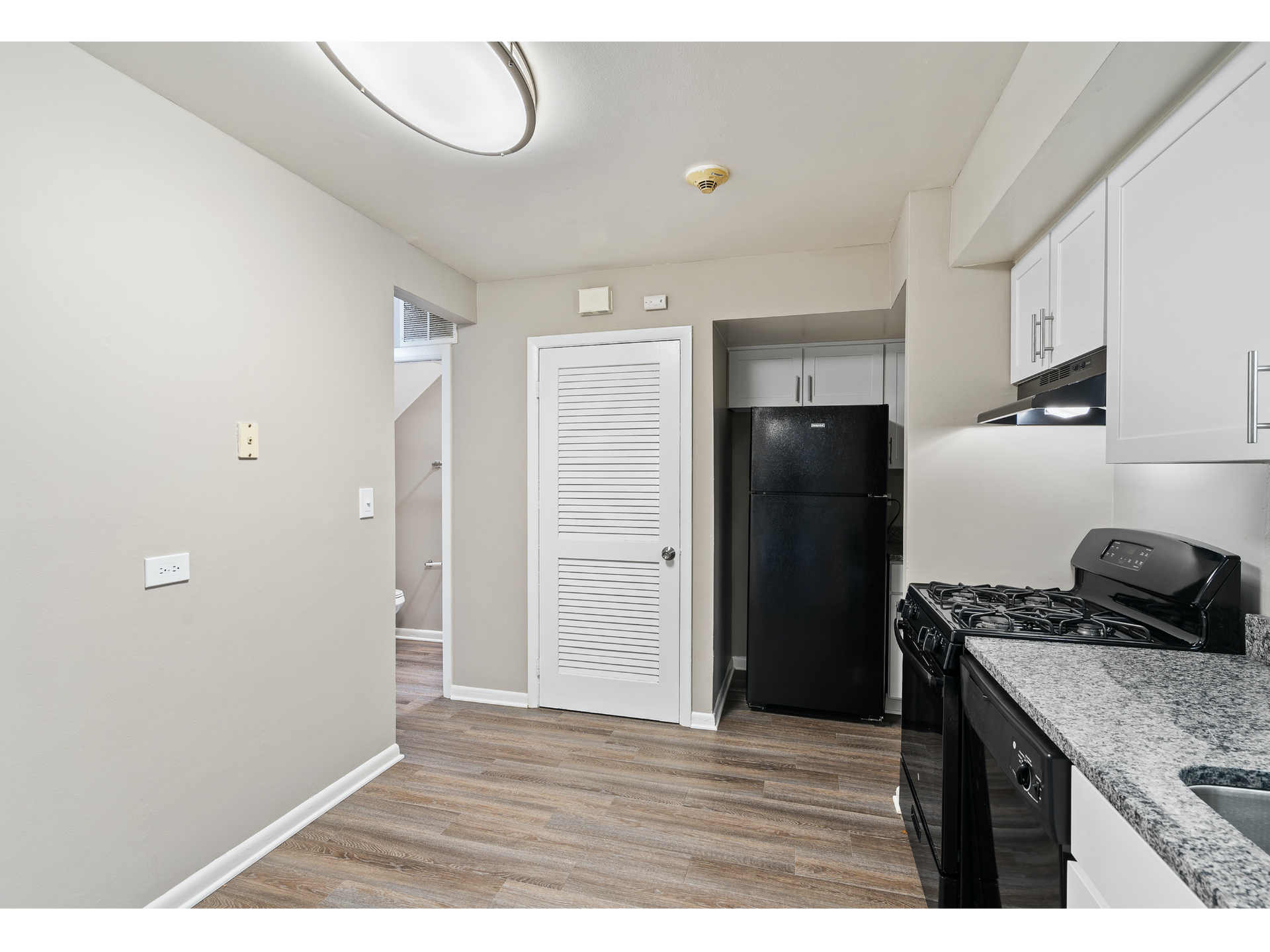 Small kitchen with white cabinets, black appliances, granite counters, and wood-look flooring.