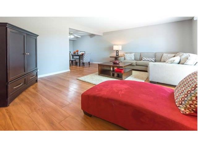 Bright living room with red ottoman, beige sofa, dark cabinet, and wood floors