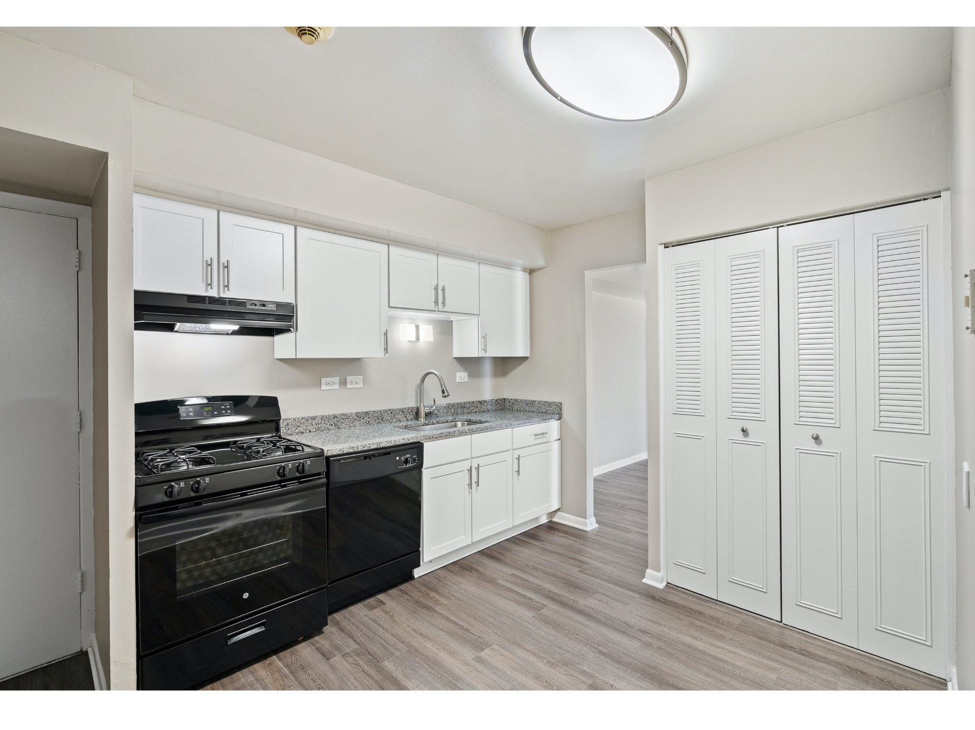 Small white kitchen with black appliances, gray countertops, and louvered closet doors.