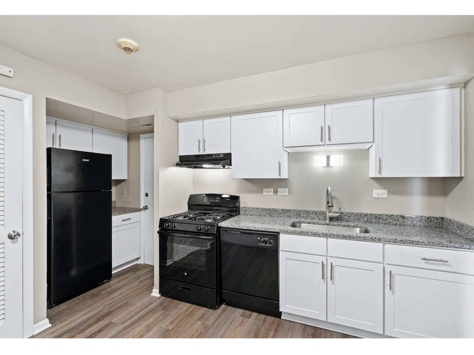 Small white kitchen with black appliances, white cabinets, and wood-look flooring.