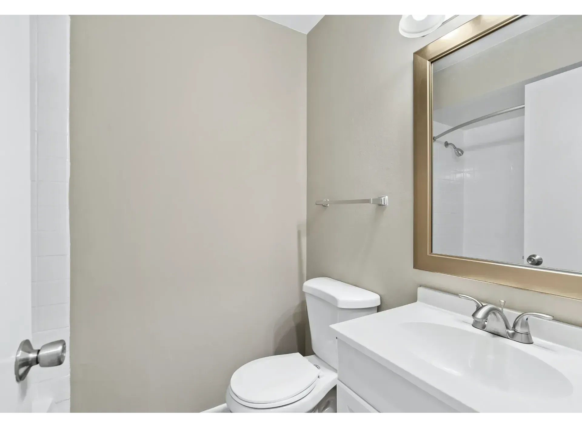 Small bathroom with toilet, sink, mirror, and towel bar on beige walls.