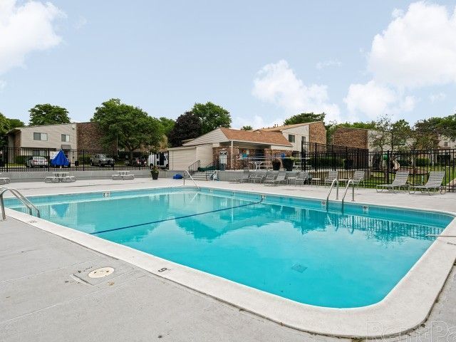 Outdoor apartment pool with turquoise water, lounge chairs, and trees on a sunny day