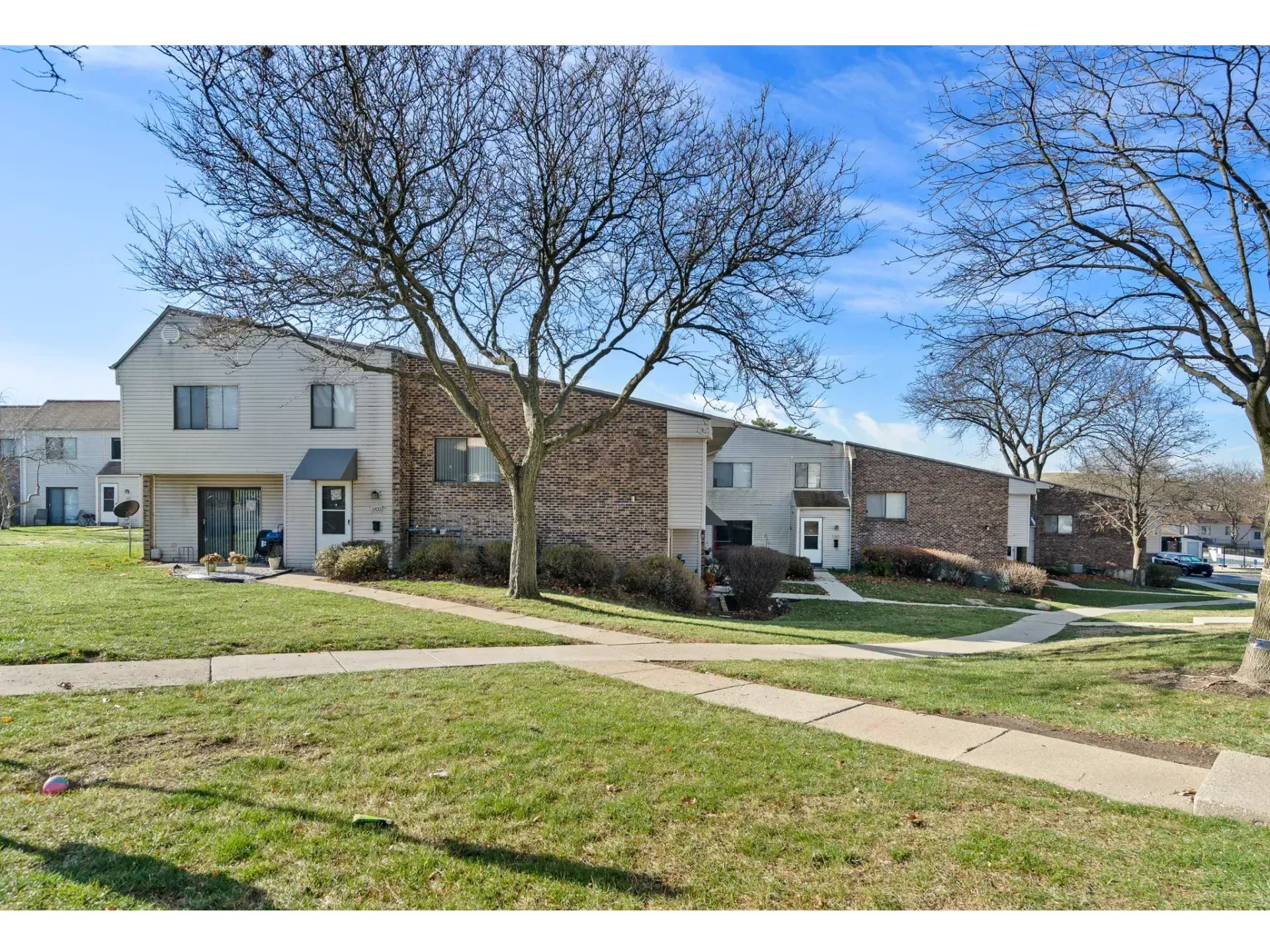 Suburban apartment buildings with leafless trees, green lawn, and sidewalks on a clear day