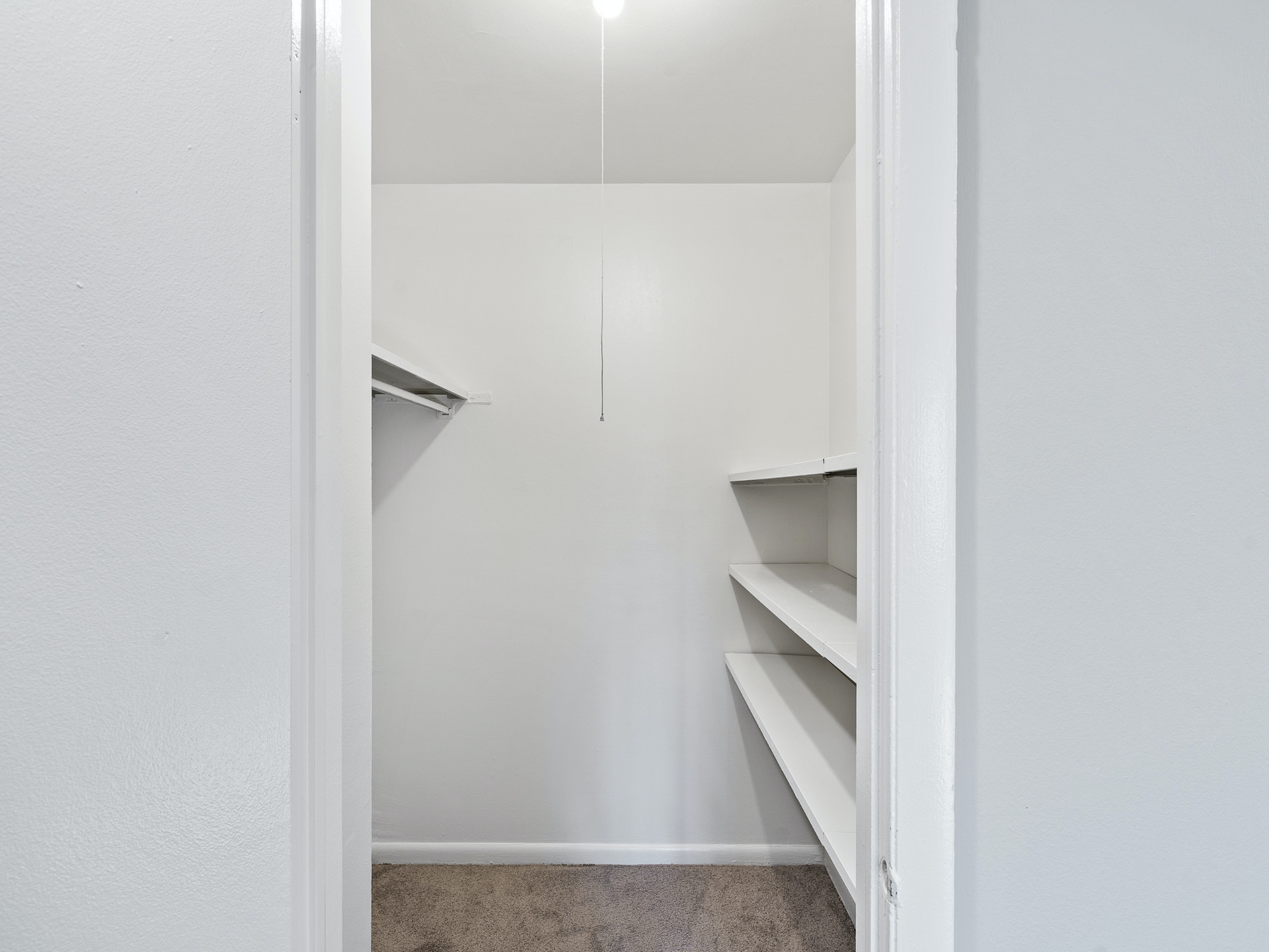 Empty white closet with built-in shelves and hanging rods, viewed through open doors.
