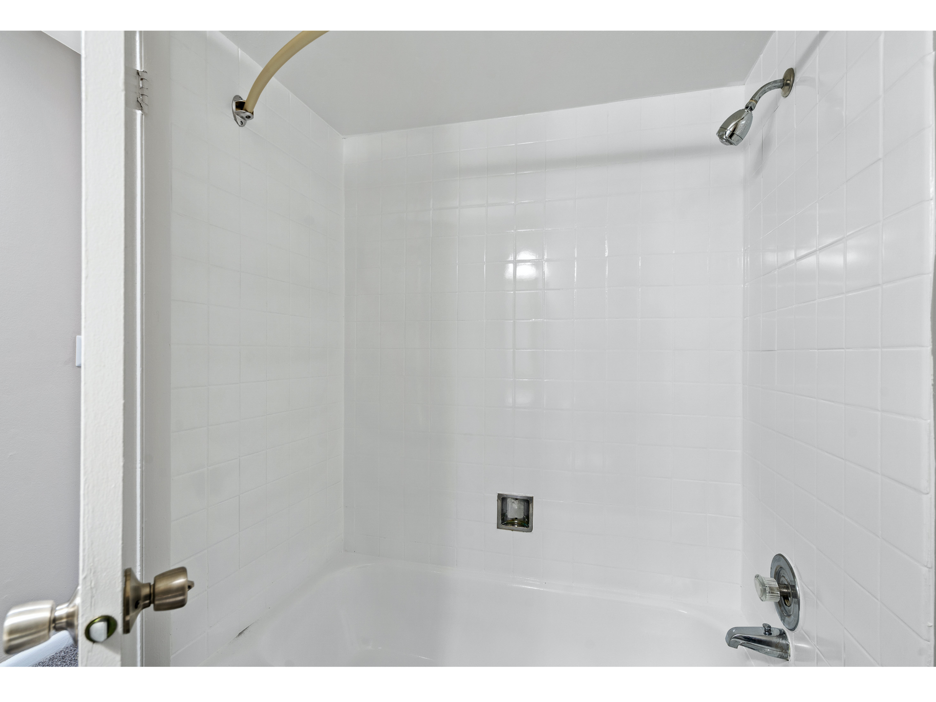 Empty white tiled shower with chrome fixtures and a bathtub faucet