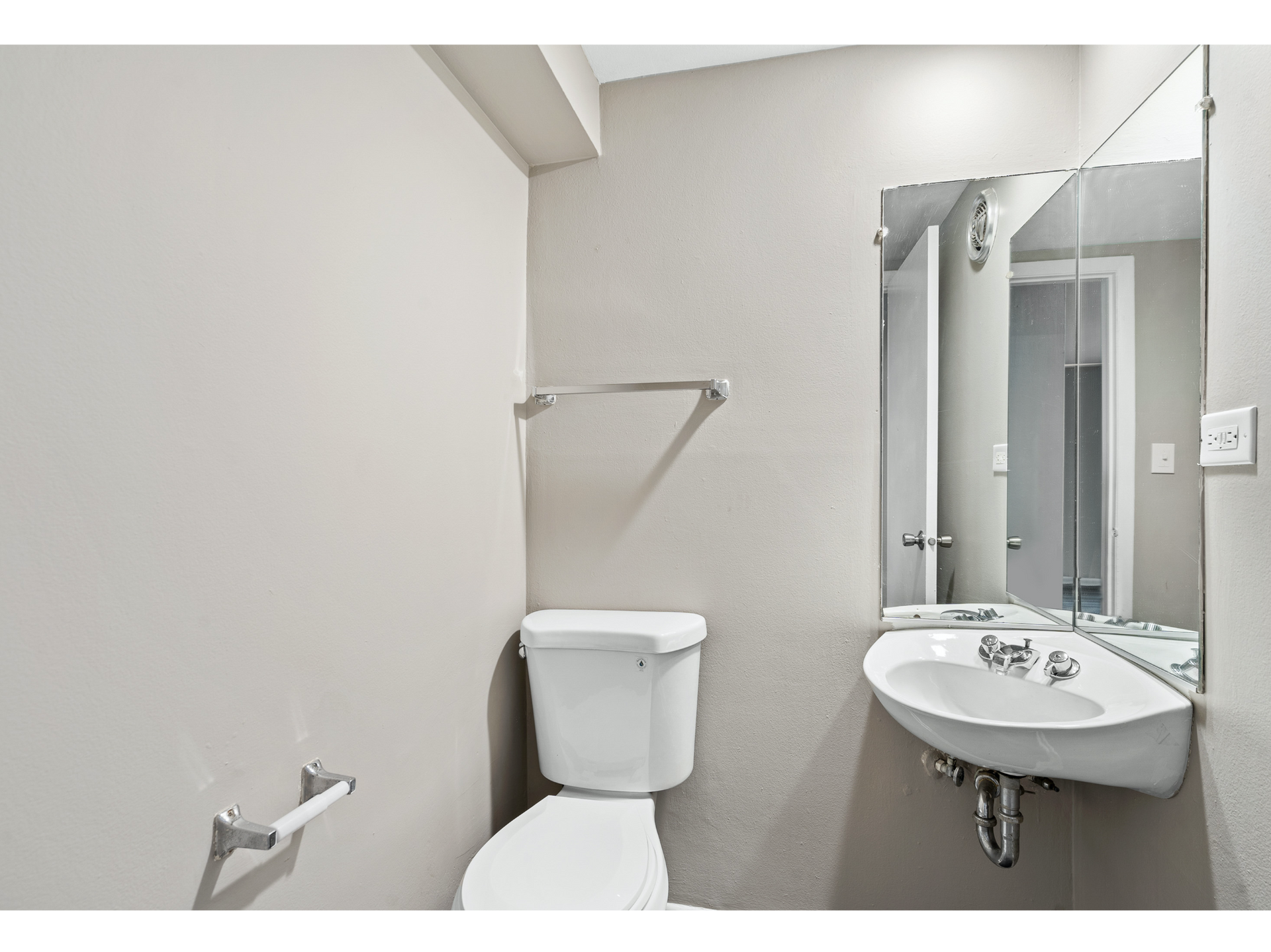 Small white bathroom with toilet, wall-mounted sink, mirror cabinet, and shower curtain