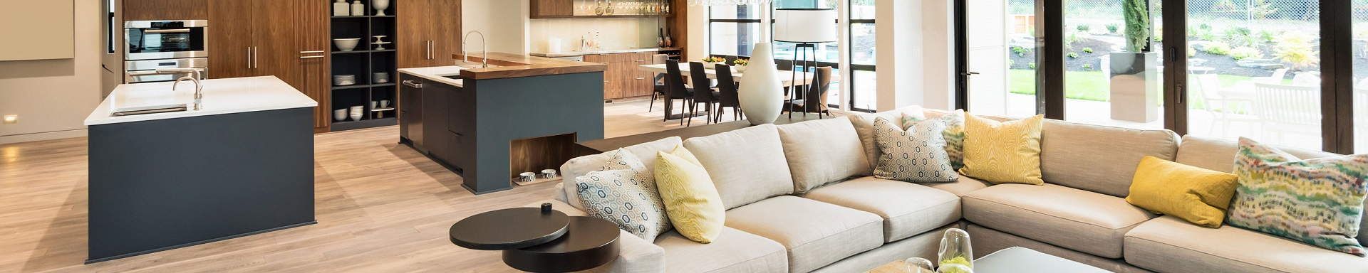 Modern living room with a beige sectional sofa, round coffee table, and open kitchen island with stools