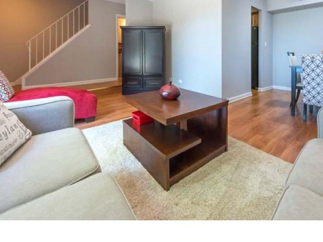 Living room with beige sofa, wooden coffee table, red ottoman, and hardwood floors