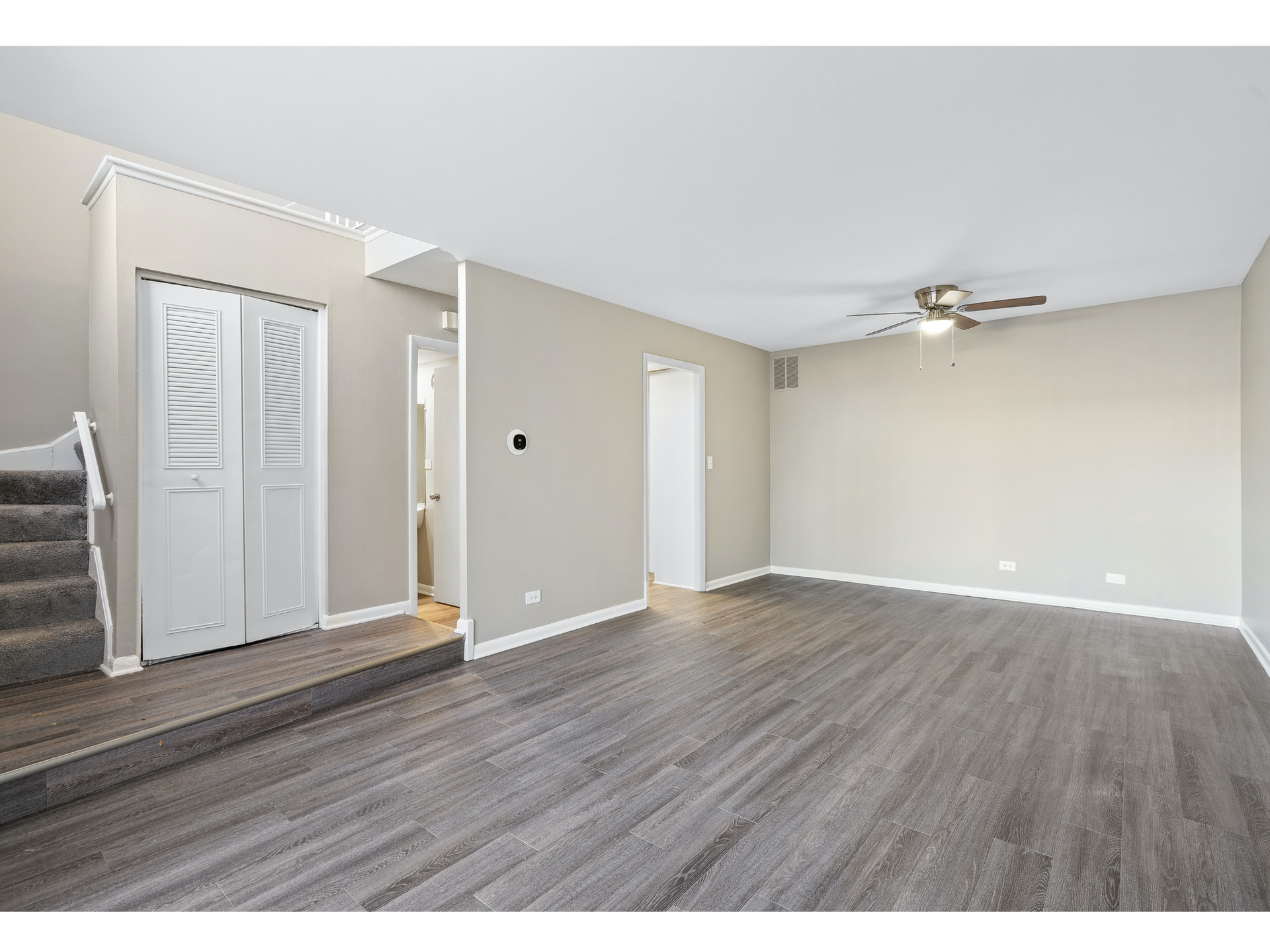 Empty beige living room with gray wood-look floors, stairs, and a white closet door