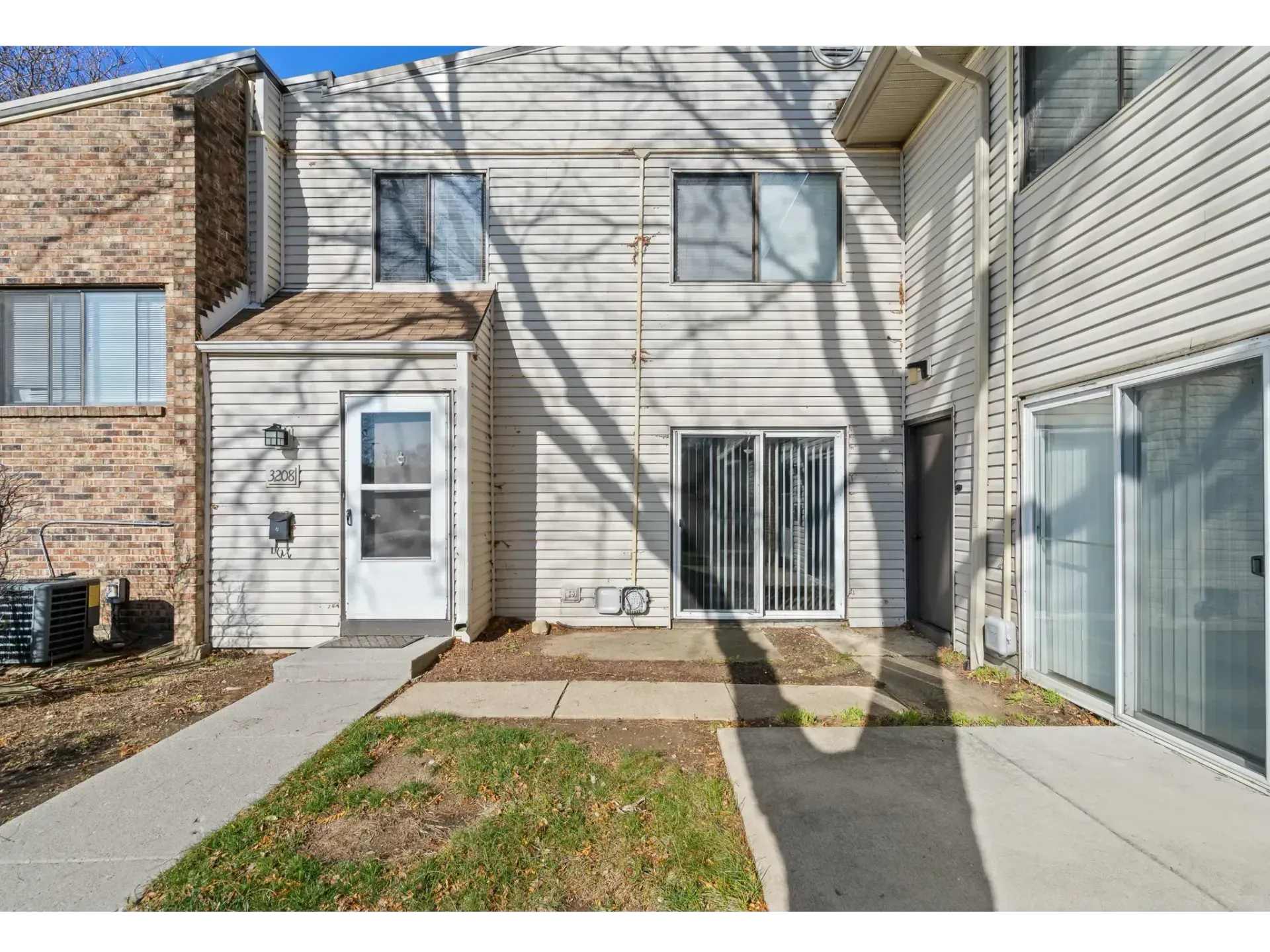 Townhouse exterior with white siding, front door, windows, and small lawn with walkway and patio.