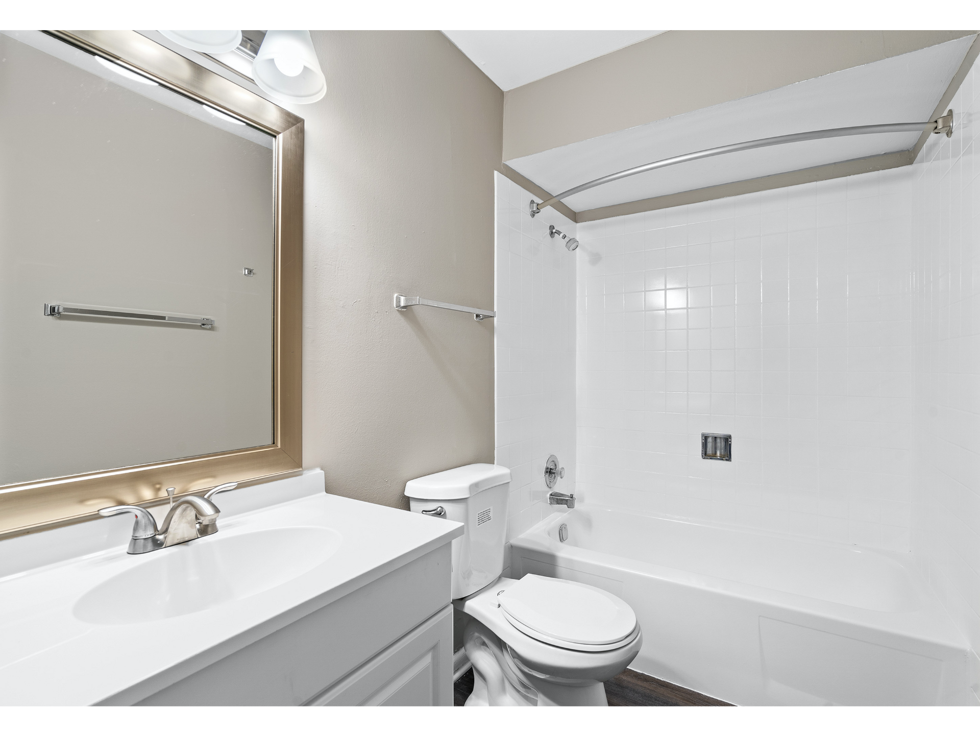 Small bathroom with white vanity, toilet, and shower-tub under a large mirror.