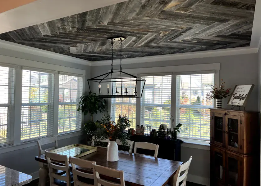 Dining room with herringbone wood ceiling, large windows, and wood dining table.