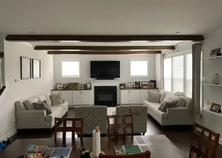 Living room with two white sofas, fireplace, dark wood beams, and built-in cabinets.
