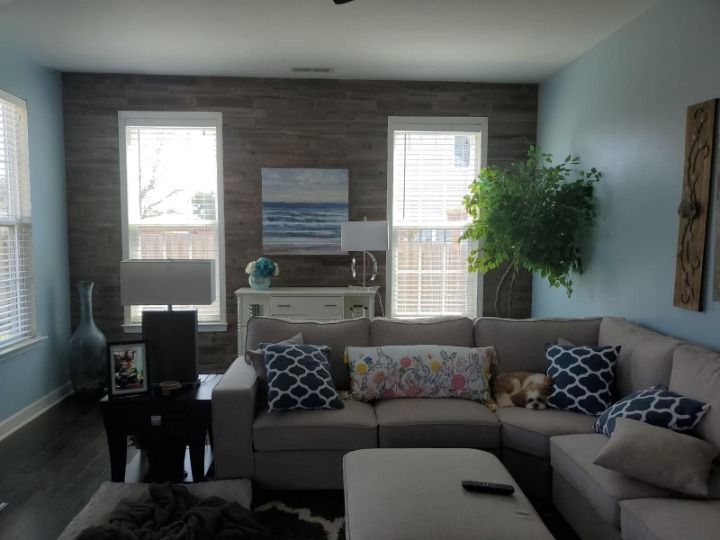 Living room with blue walls, wood accent wall, beige sectional, and windows.