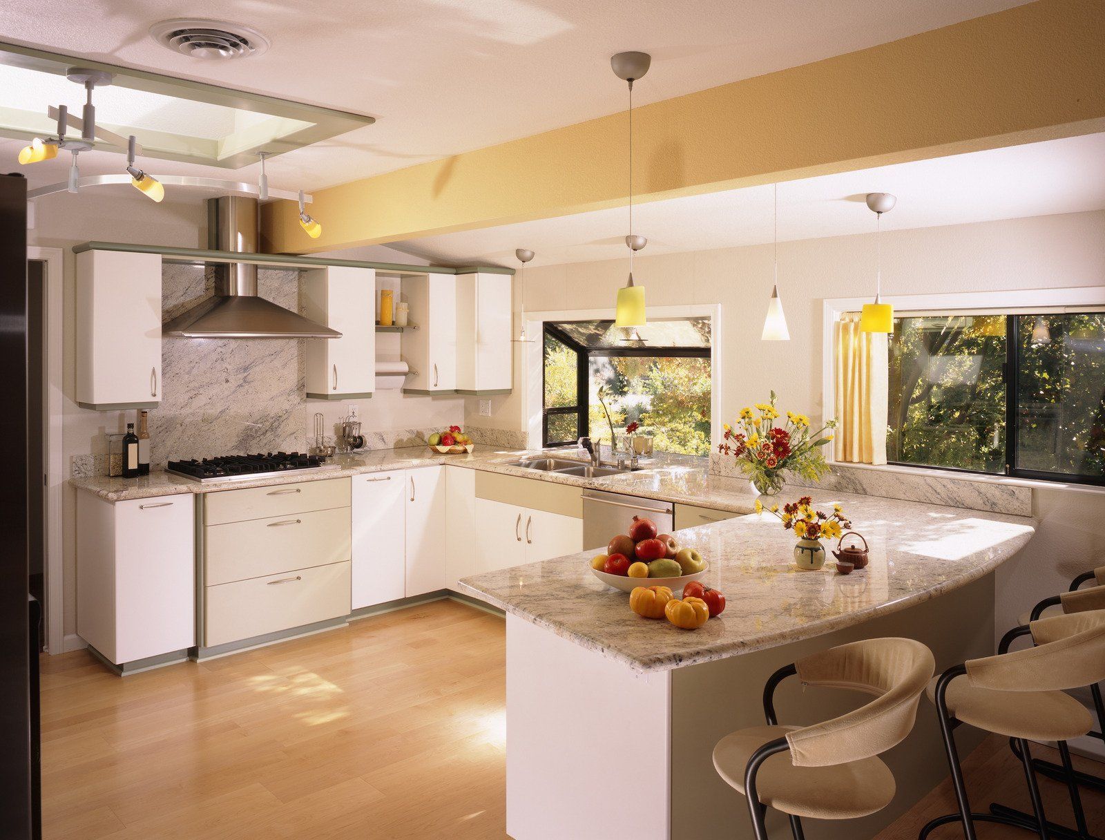 A modern, white and beige kitchen with a marble countertop island, fruit and flowers, and bar stools.
