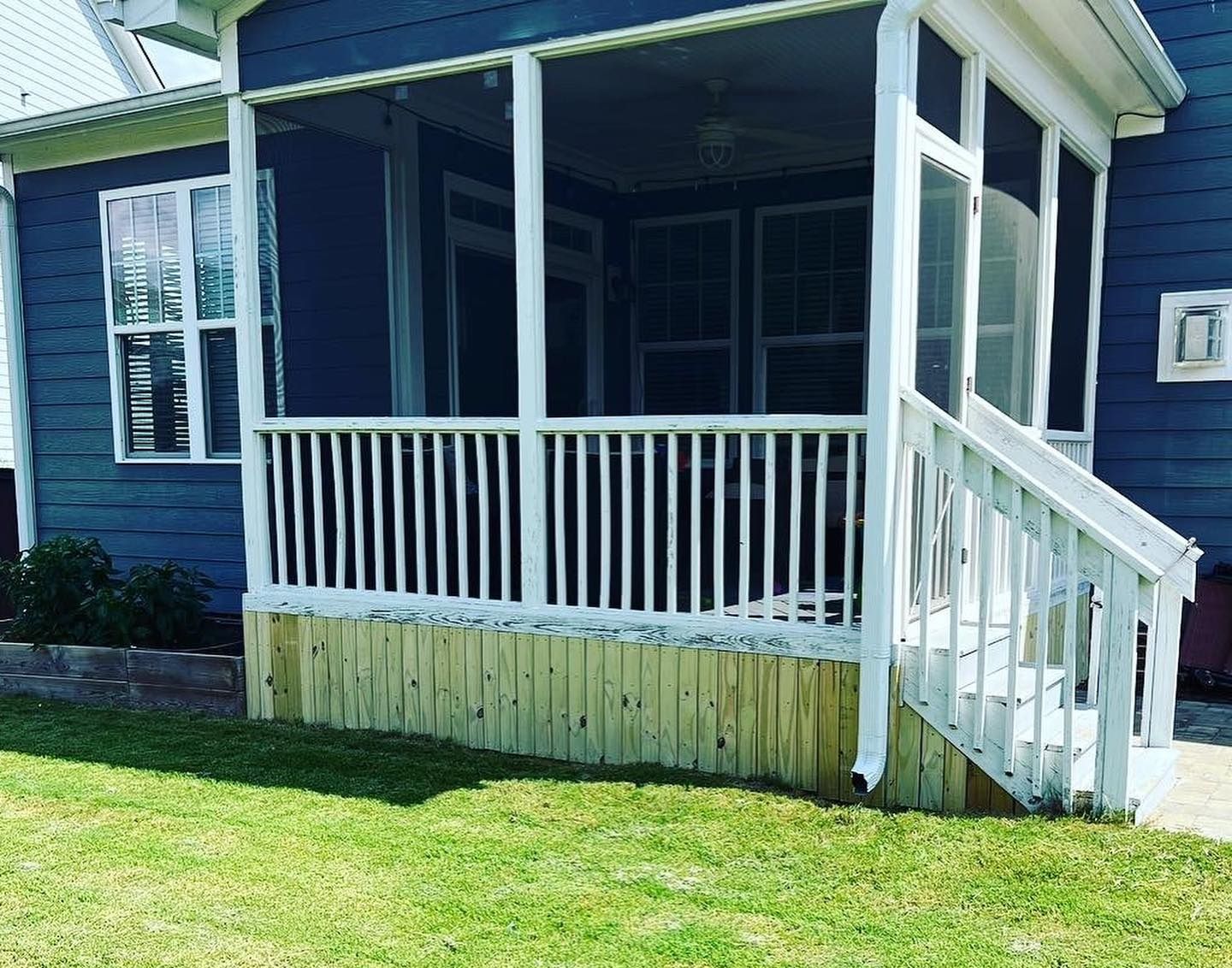 Blue house with a screened porch and white railing, set on a grassy lawn.