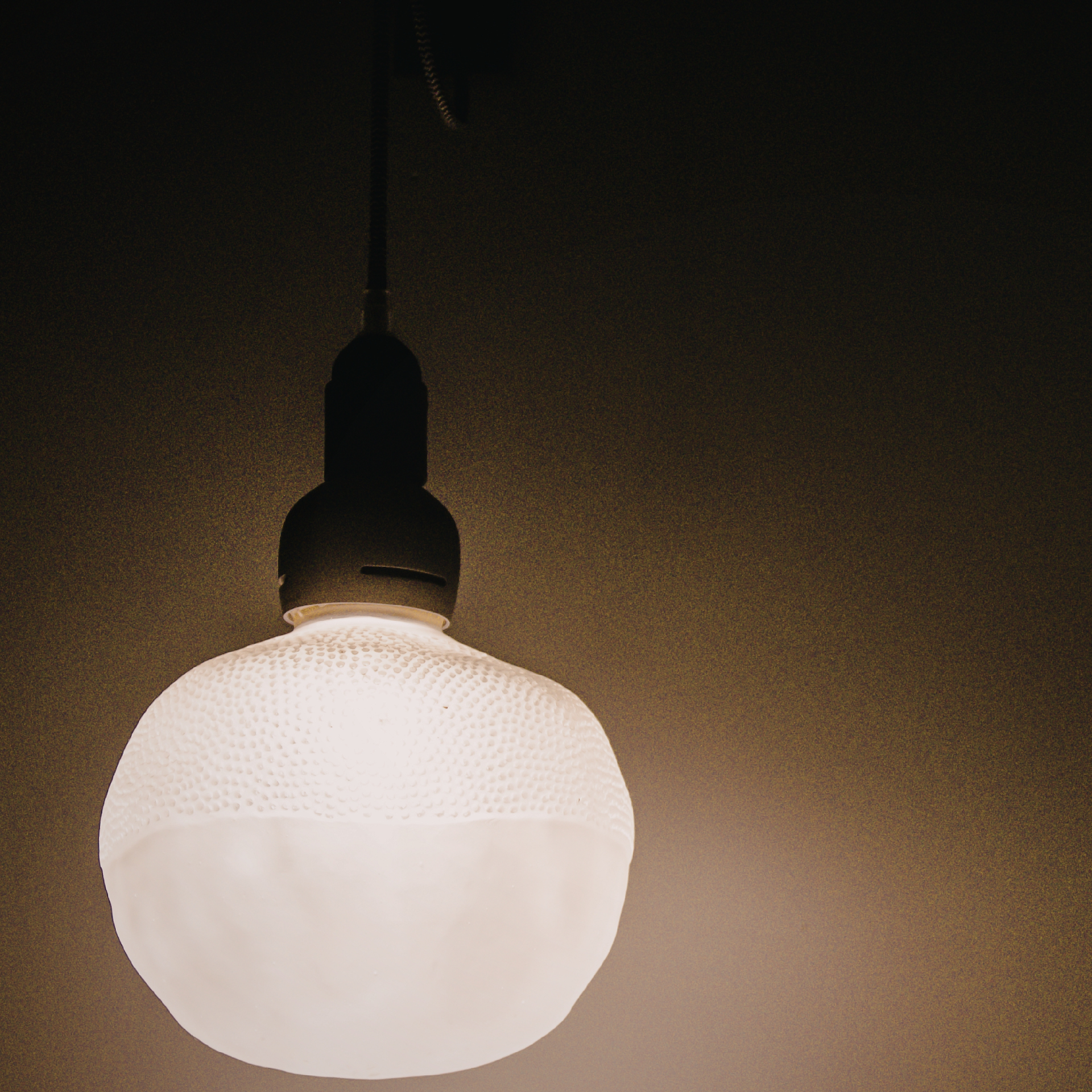 A single, round, textured pendant light glows warmly against a dark, plain background.