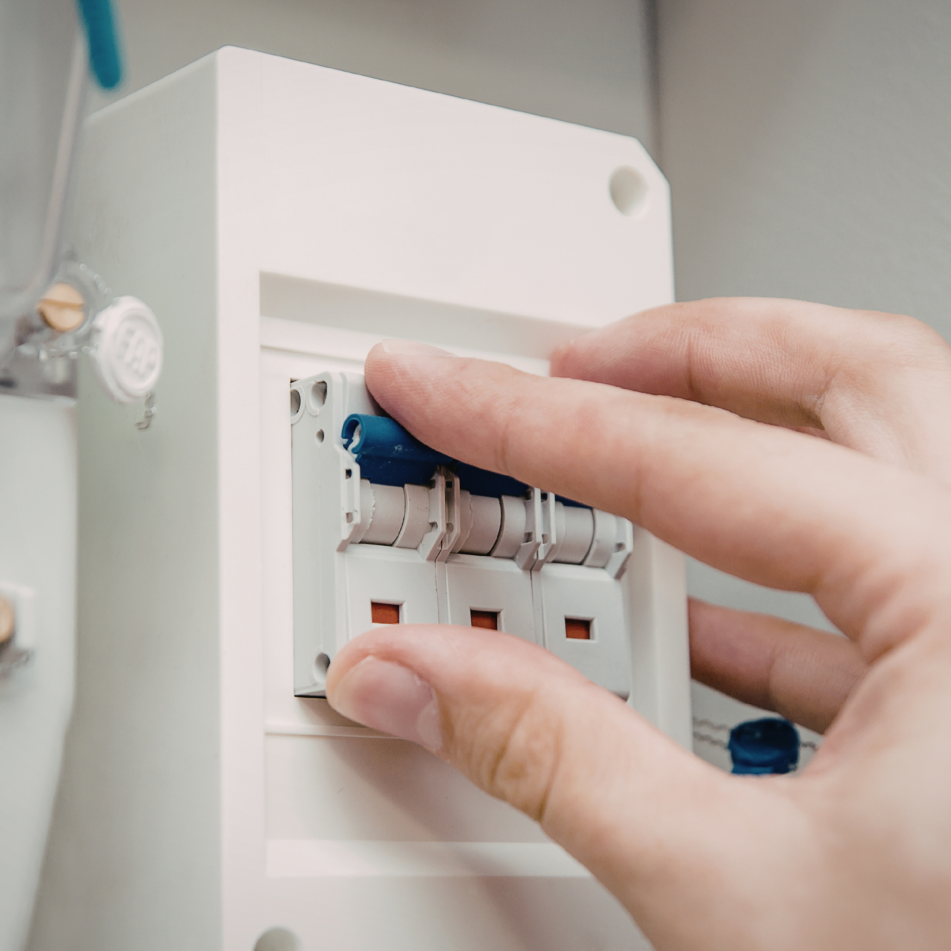 A hand flips the switches of a three-pole circuit breaker mounted in a white wall panel.