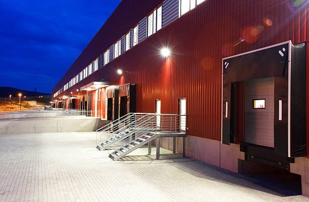 A red industrial warehouse building at night with metal loading docks and exterior staircases under bright lighting.