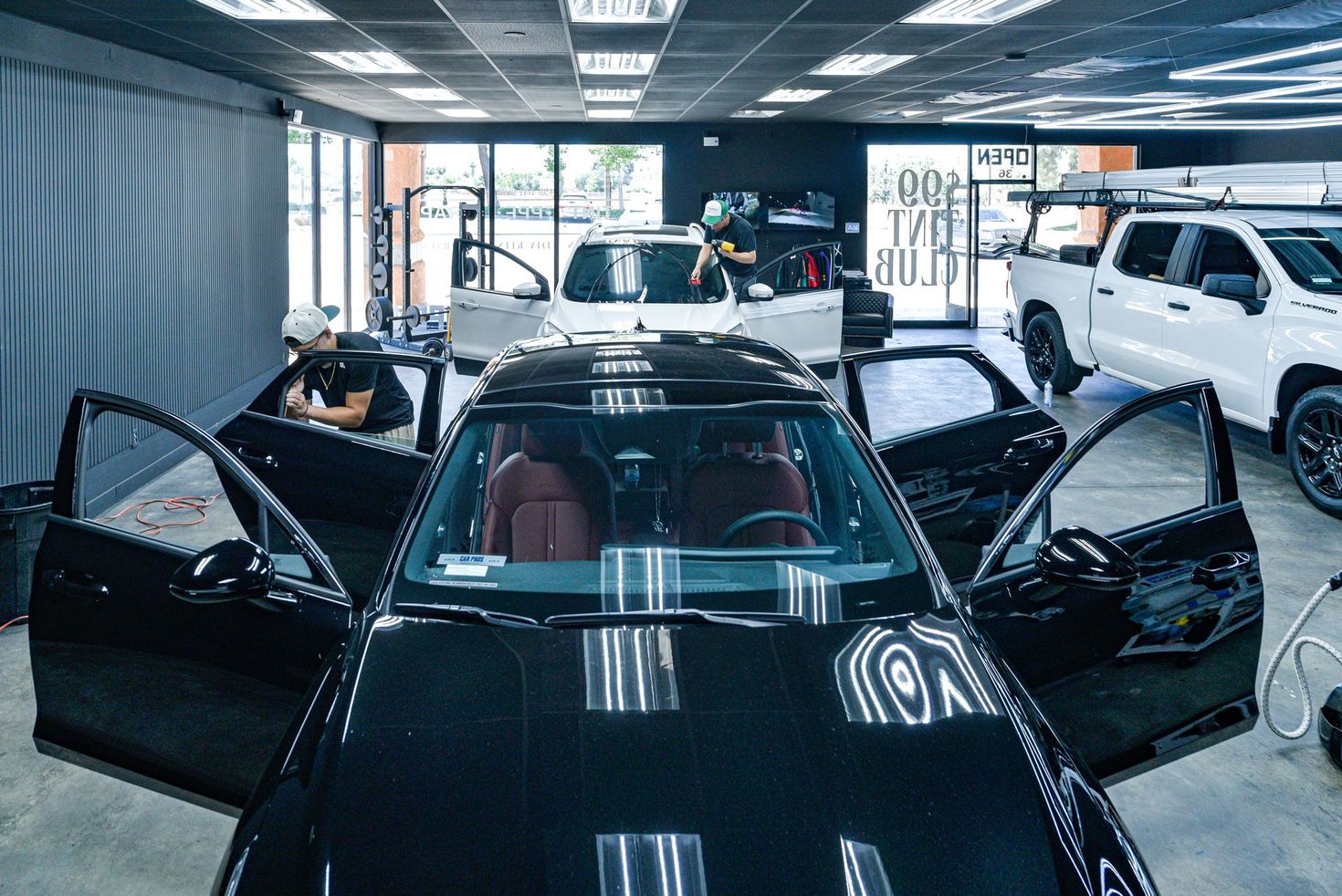 Black luxury car with doors open at 99 Tint Club in Yucaipa showroom, with a white SUV in the background.
