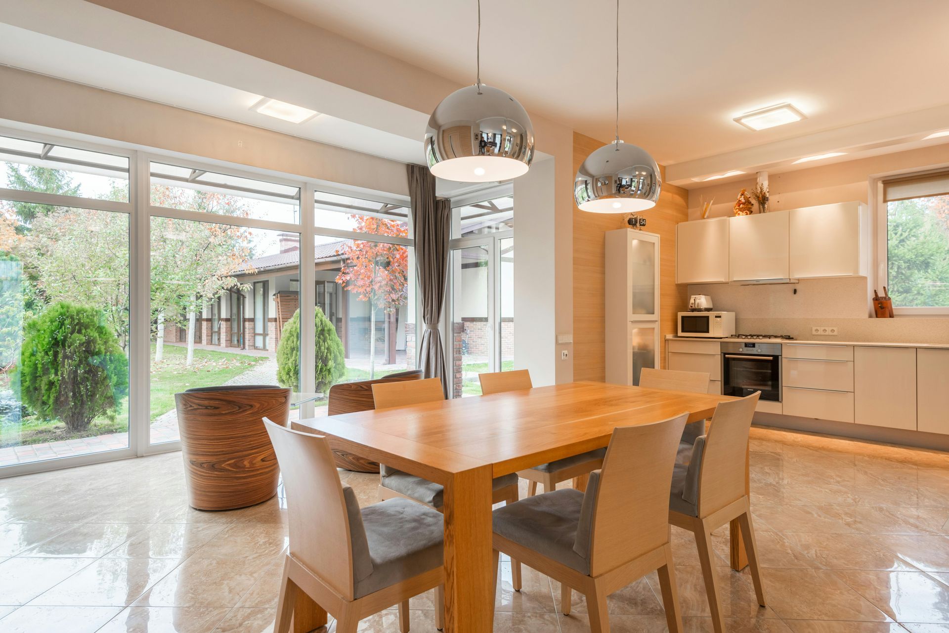 Bright open dining room with wooden table, chairs, pendant lights, and large sliding glass doors to a garden.