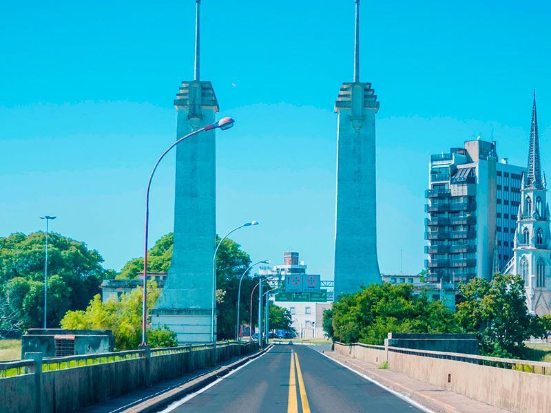 Em um dia claro e ensolarado, uma estrada asfaltada conduz a duas altas torres art déco azul-claras, com a torre de uma igreja ao longe.