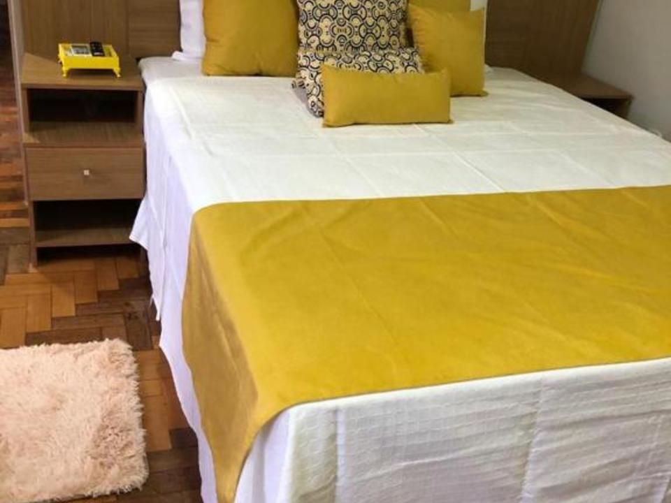 Uma cama impecavelmente arrumada com lençóis brancos, um caminho de mesa amarelo mostarda e uma coleção de almofadas amarelas e estampadas combinando.