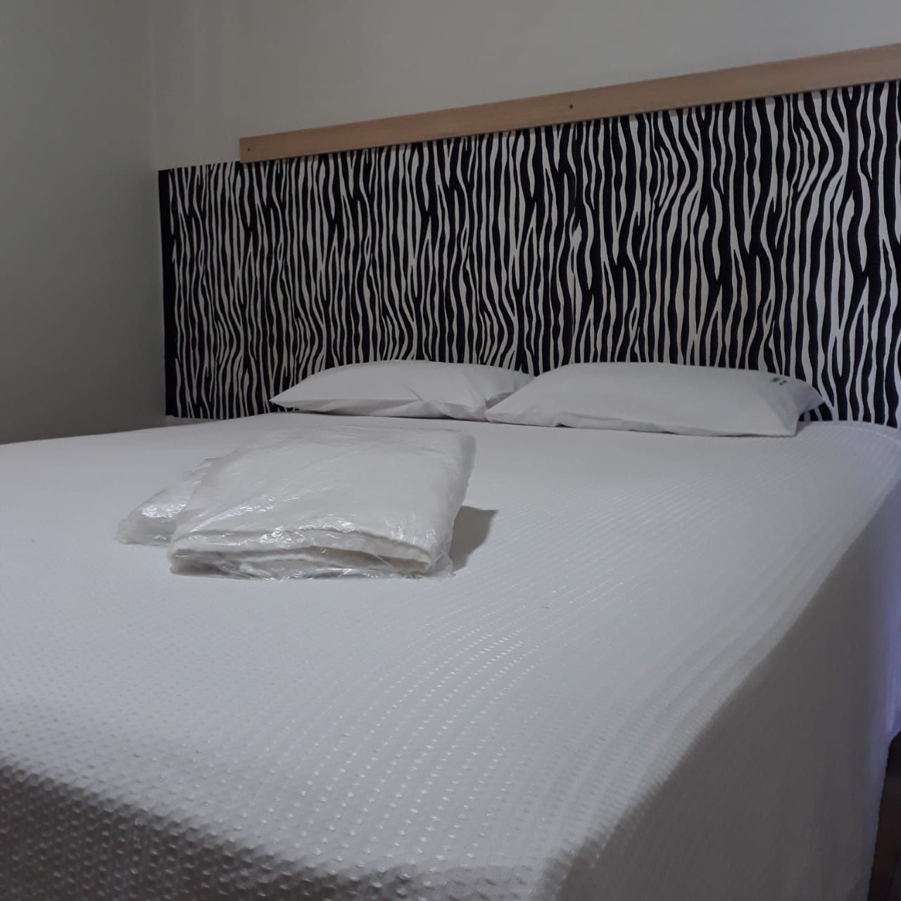 Uma cama com cabeceira estampada com zebra, roupa de cama branca, dois travesseiros e um item branco dobrado em cima.