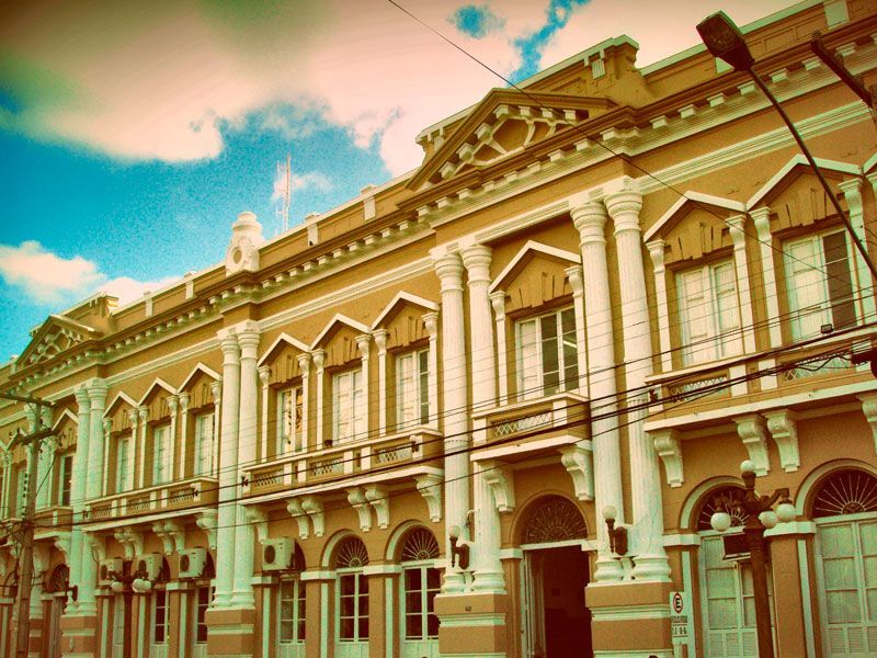 Um edifício ornamentado de vários andares em tons dourados quentes com colunas brancas, detalhes neoclássicos e janelas em arco.