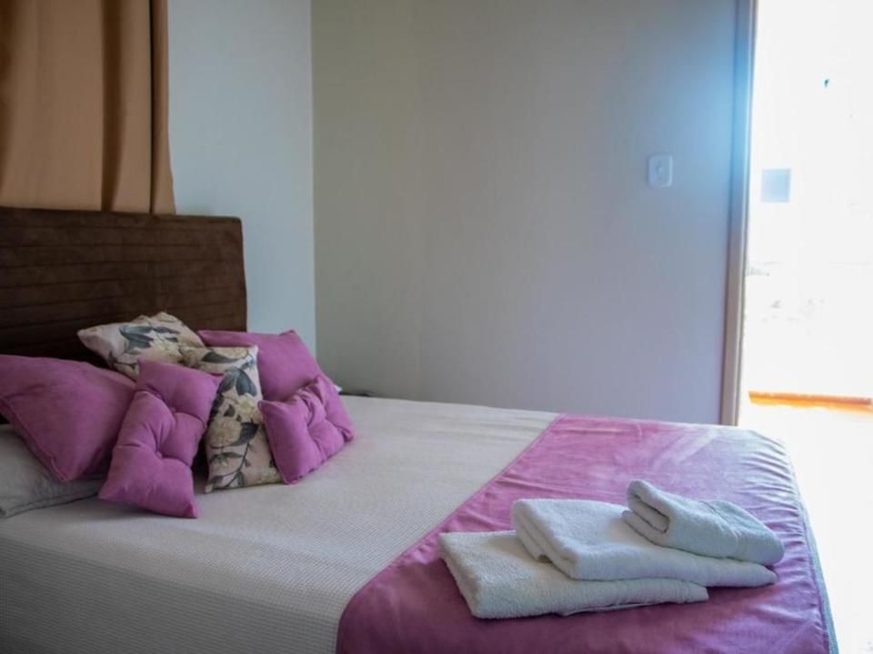 Uma cama estilo hotel com lençóis brancos, travesseiros rosa e cabeceira de madeira, com toalhas dobradas aos pés da cama.