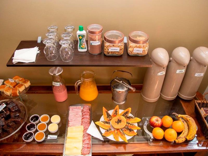 Um buffet de café da manhã de hotel com doces, frutas, frios, bebidas e diversos potes dispostos em superfícies de madeira de vários níveis.