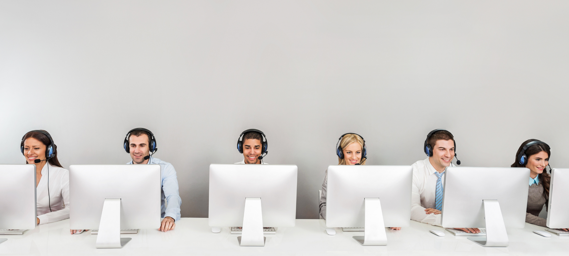 Row of office workers wearing headsets behind desktop monitors on a white background