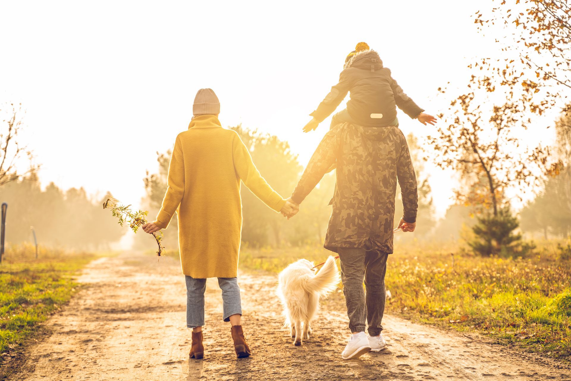 Two people walking a dog on a sunlit path in autumn fields