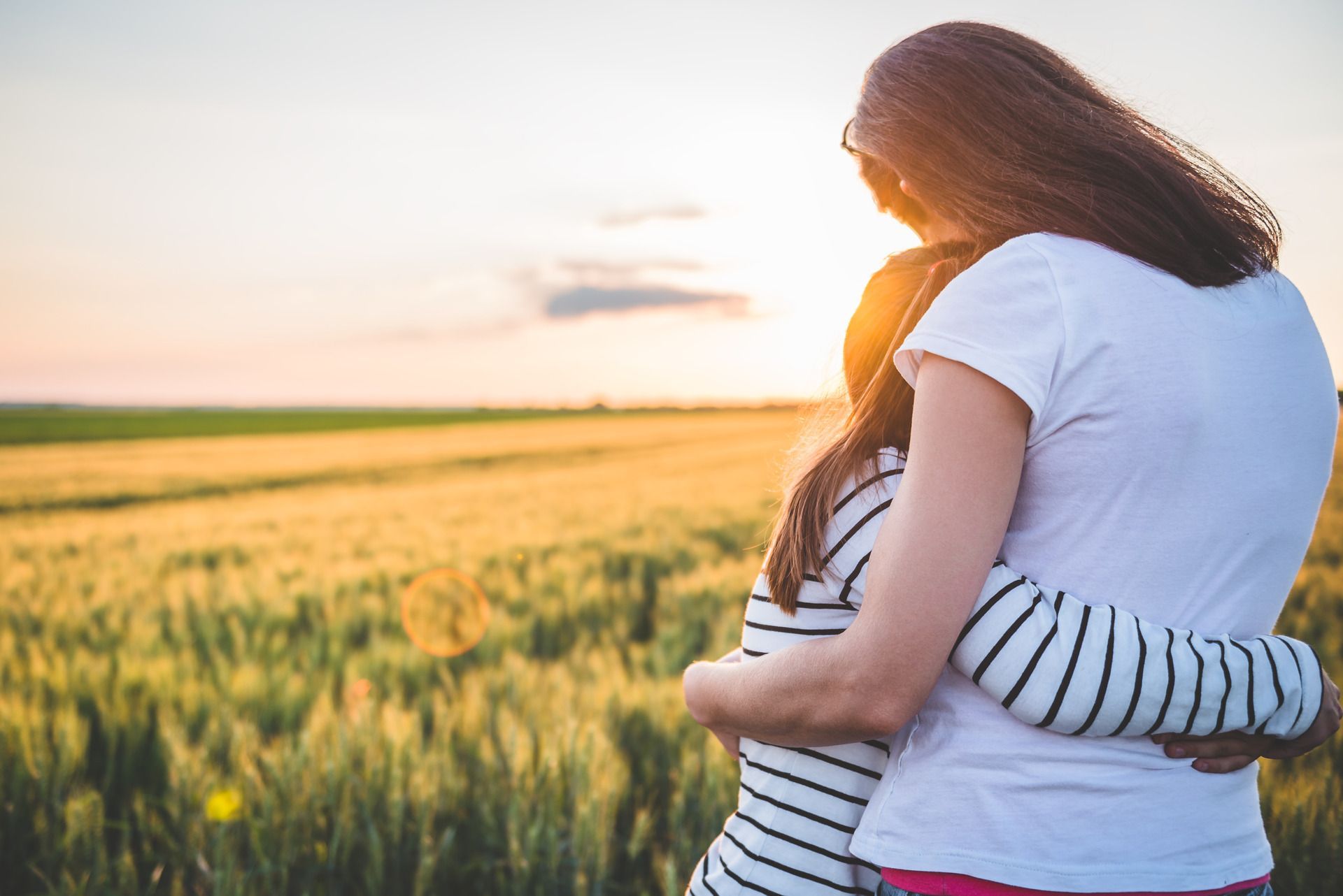 Two people hugging in a sunlit field at sunset