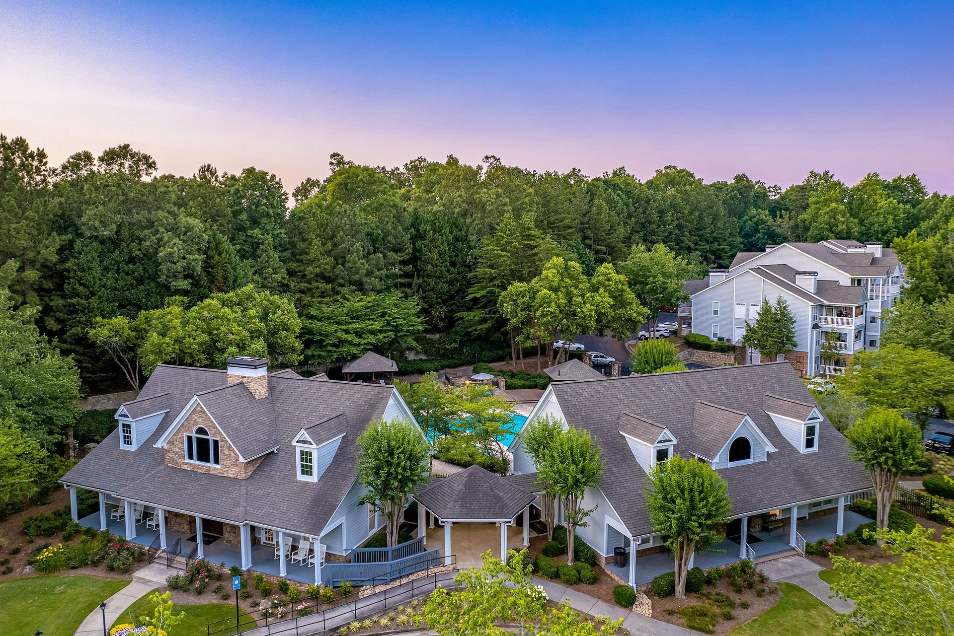 Two-story blue and white buildings with wrap-around porches, near a pool, surrounded by trees, under a blue sky at Marquis at Sugarloaf, offers apartments for rent in Duluth, GA.