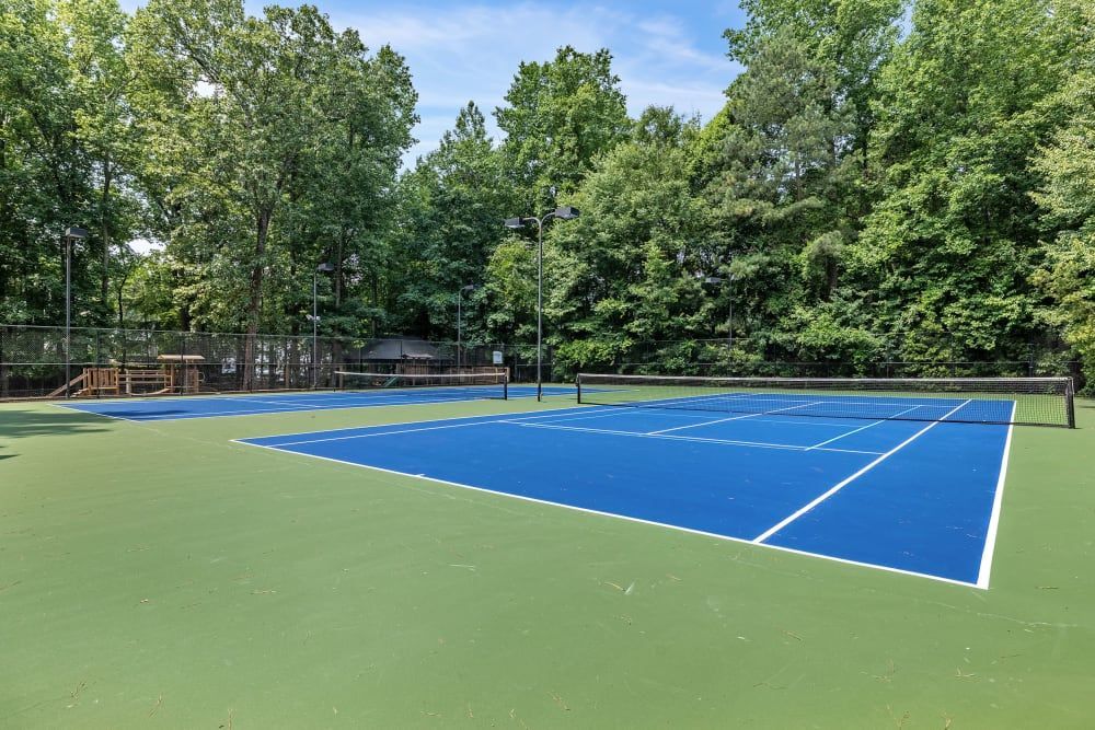 Blue and green tennis courts surrounded by trees on a sunny day at Marquis at Sugarloaf, offers apartments for rent near Sugarloaf Mills.