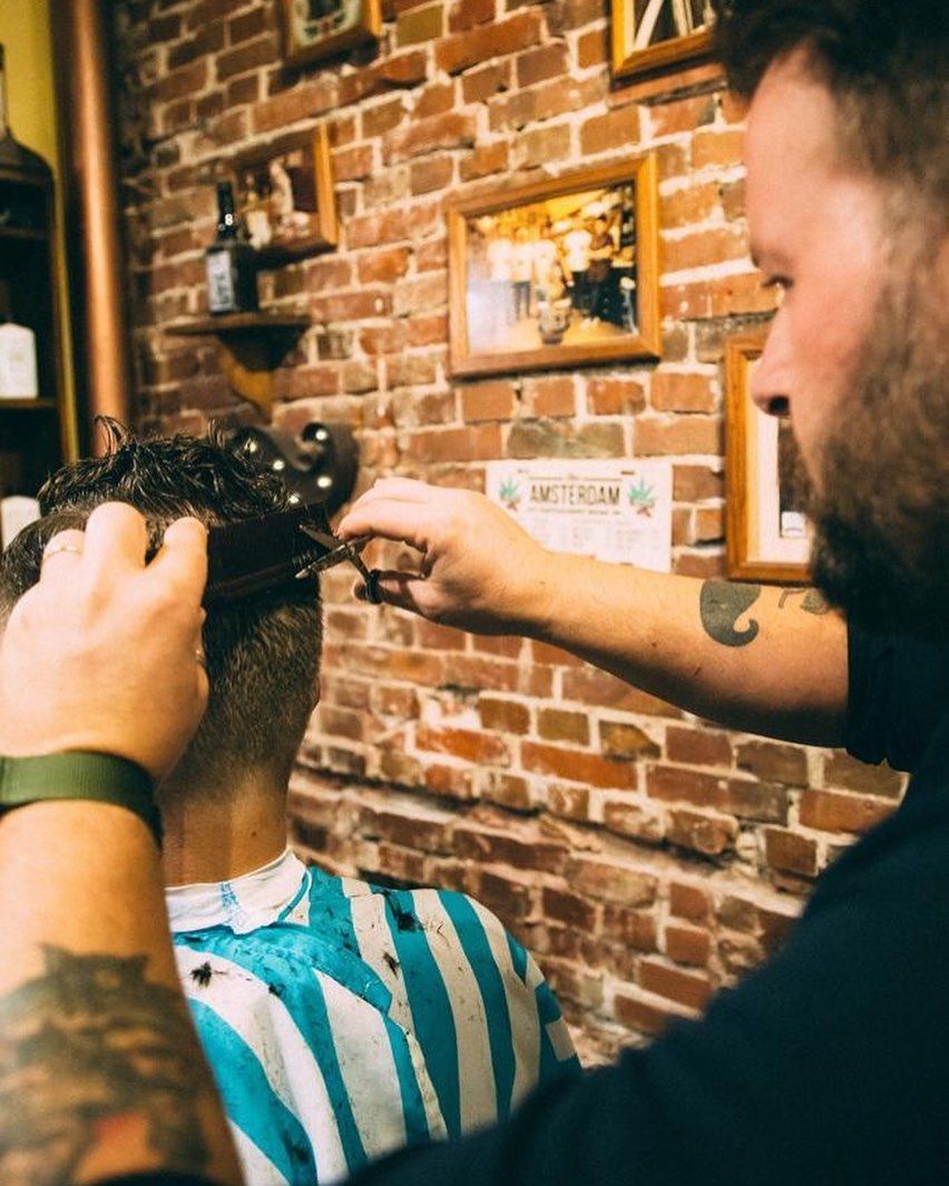 Un uomo si sta facendo tagliare i capelli dal barbiere davanti a un muro di mattoni.