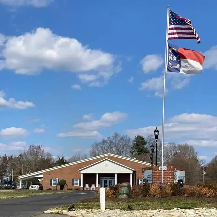 Brick community building with two flags flying under a blue sky with clouds.