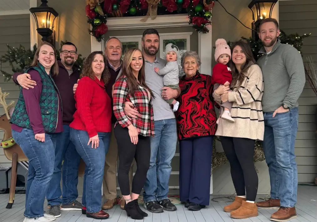 Group of people posing on a porch decorated with holiday garland and lanterns, smiling at the camera