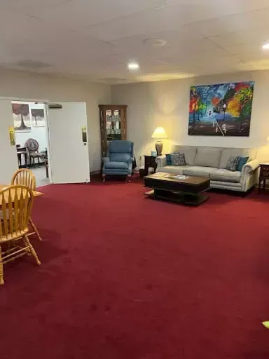 Spacious living room with red carpet, gray sofa, blue recliner, coffee table, lamp, and colorful wall art.