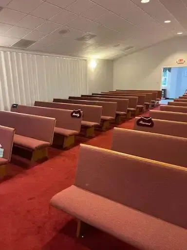 Empty church sanctuary with pink pews, red carpet, and white ceiling panels, viewed toward the front aisle