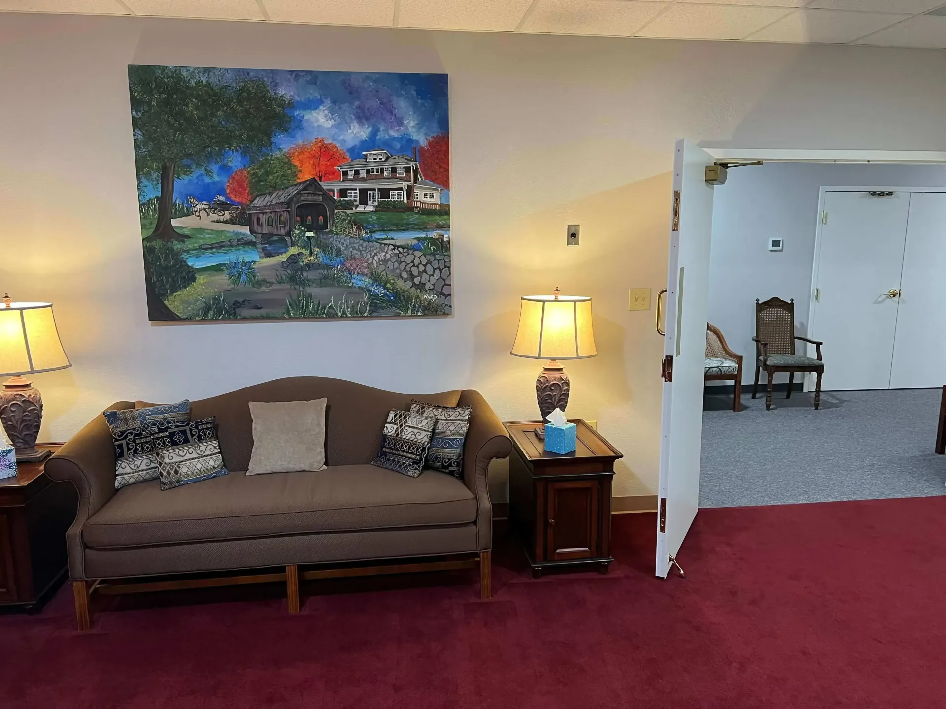 Living room with brown sofa, lamps, colorful wall art, and an open doorway to a dining area