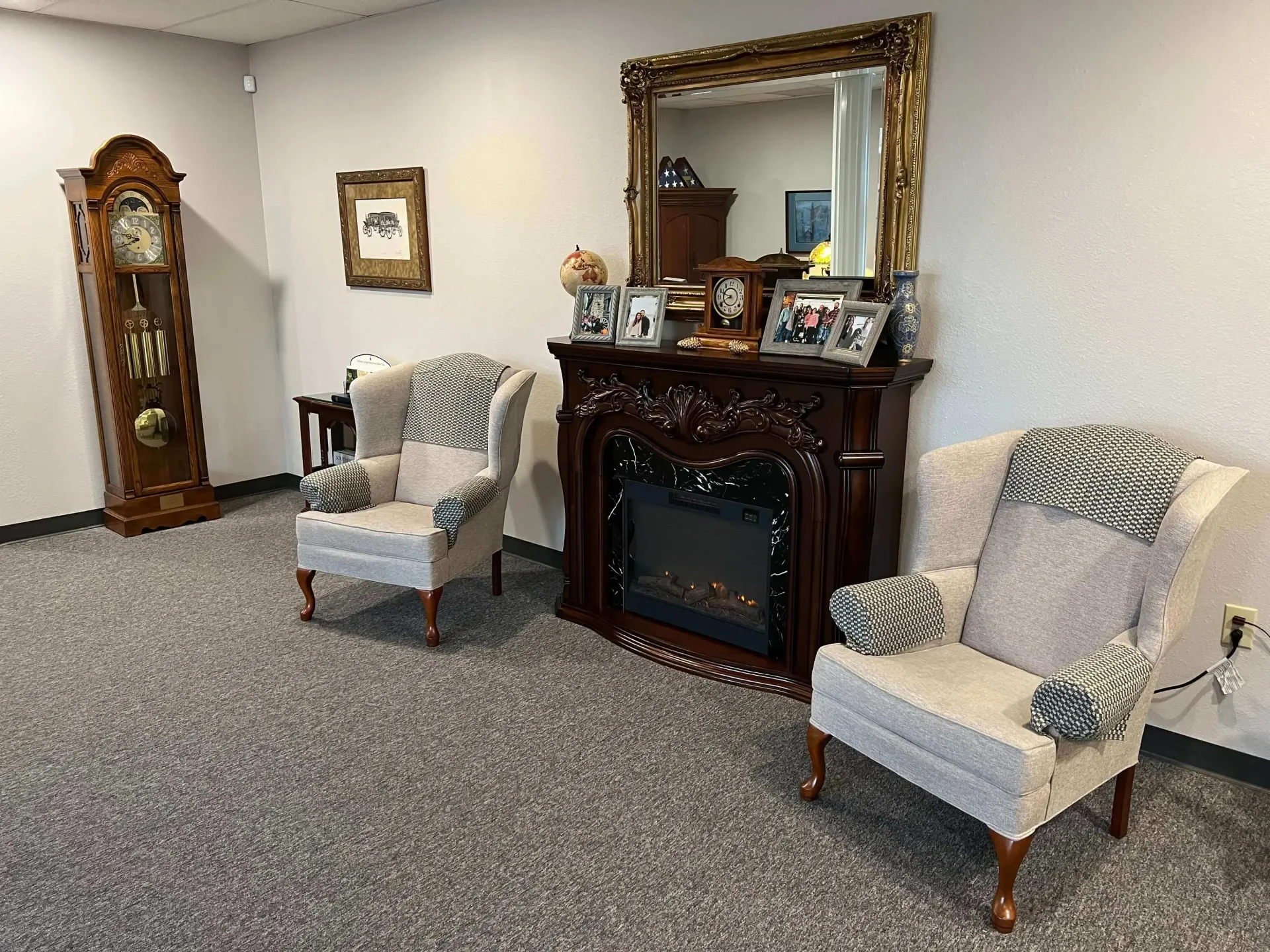 Elegant living room with fireplace, mirror, grandfather clock, and two patterned armchairs on gray carpet