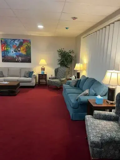Quiet lounge with red carpet, blue sofas, lamps, and framed artwork along the wall.