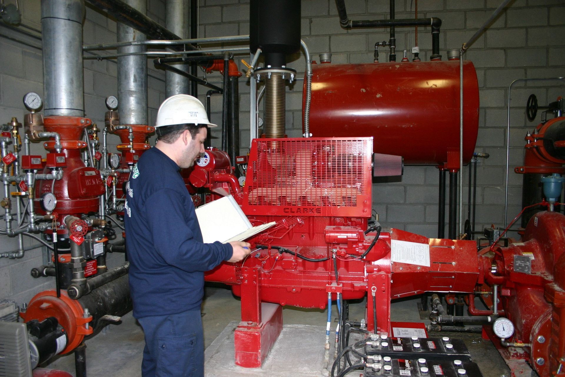 Un homme portant un casque de chantier inspecte une pompe à incendie rouge dans un local technique.
