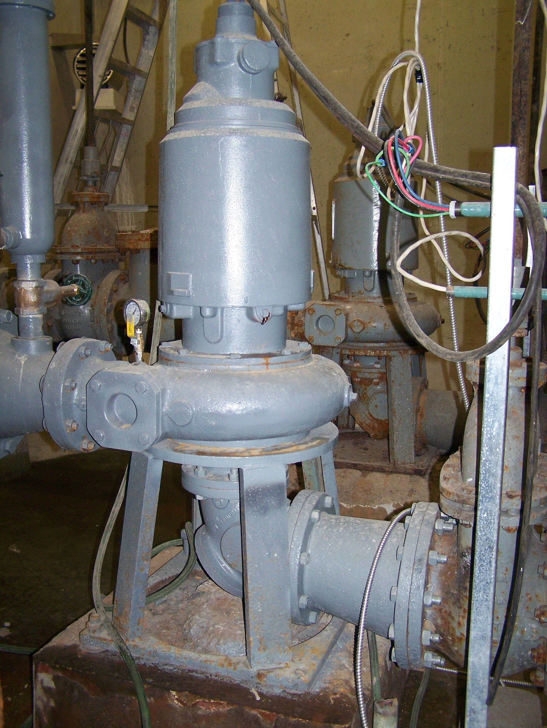 Pompe industrielle grise avec moteur vertical, tuyaux et câblage électrique.