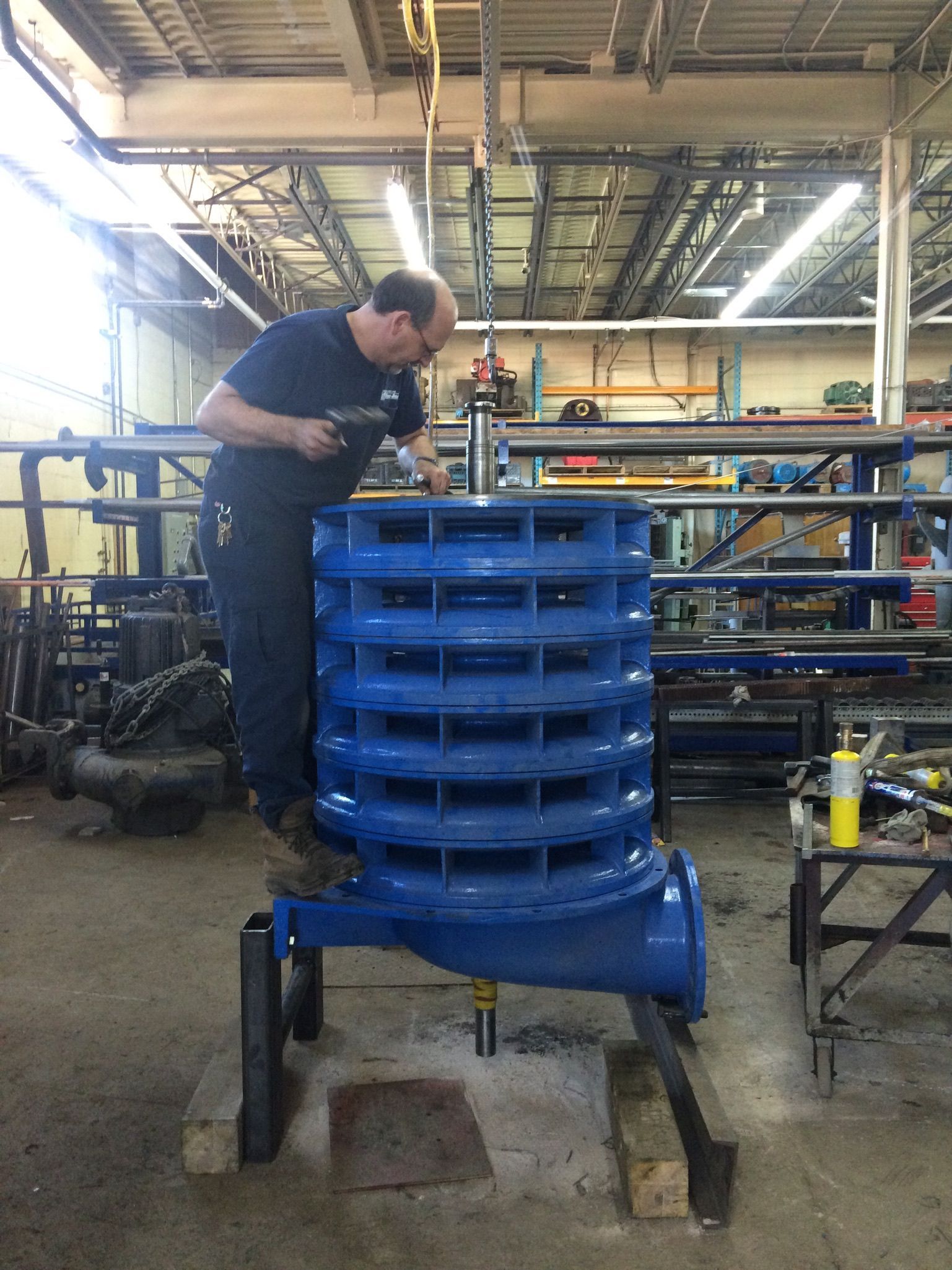 Dans un atelier, une personne travaille sur une grande pompe industrielle bleue.