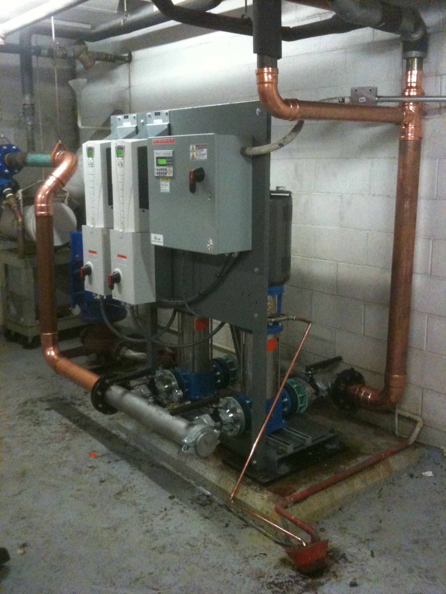 Système de pompage d'eau industriel avec tuyauterie en cuivre, panneaux de commande et équipements installés en sous-sol.